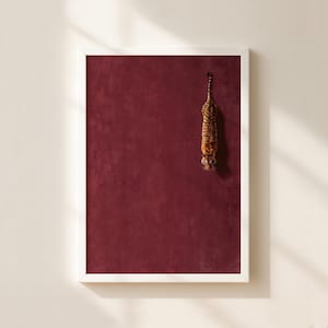 May include: A framed vertical wall art print featuring a deep burgundy textured background with a small, detailed illustration of a tiger positioned in the upper right quadrant, oriented vertically with its head pointing downward toward the bottom.
