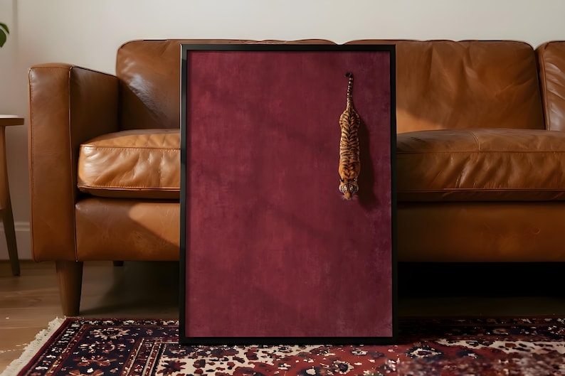 May include: A rectangular wall art piece featuring a deep burgundy velvet-textured background enclosed in a thin black frame. A small, detailed figurine of a tiger is attached to the upper right side, hanging vertically with its head facing downward.
