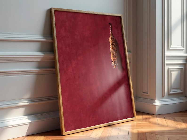 May include: A rectangular wall art piece in a light wood frame featuring a deep crimson red background with a textured finish. A small, detailed illustration of a tiger is positioned in the upper right quadrant, appearing to descend vertically.