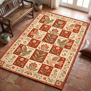 Könnte beinhalten: Ein rechteckiger Teppich mit einem sich wiederholenden Gittermuster aus abwechselnden Quadraten. Das Design zeigt stilisierte Vögel und florale Motive in Terrakotta-Rot, Creme und Salbeigrün, eingefasst von einer dekorativen botanischen Bordüre.