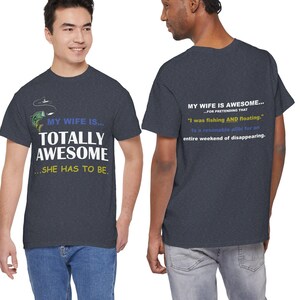 May include: A dark heather gray short-sleeve t-shirt featuring a graphic on the front that reads "MY WIFE IS... TOTALLY AWESOME...SHE HAS TO BE." with a fish illustration. The back displays the text "MY WIFE IS AWESOME... FOR PRETENDING THAT "I was fishing AND floating." is a reasonable alibi for an entire weekend of disappearing."
