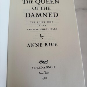 May include: Open book page with the title "THE QUEEN OF THE DAMNED" by Anne Rice. The text is in black font on an off-white page. The book is part of "THE VAMPIRE CHRONICLES" series, published by Alfred A. Knopf in 1988.