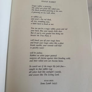 May include: Open book page with the poem "Tragic Rabbit" by Stan Rice. The text is in black font on a cream-colored page. The poem's title and author's name are visible.