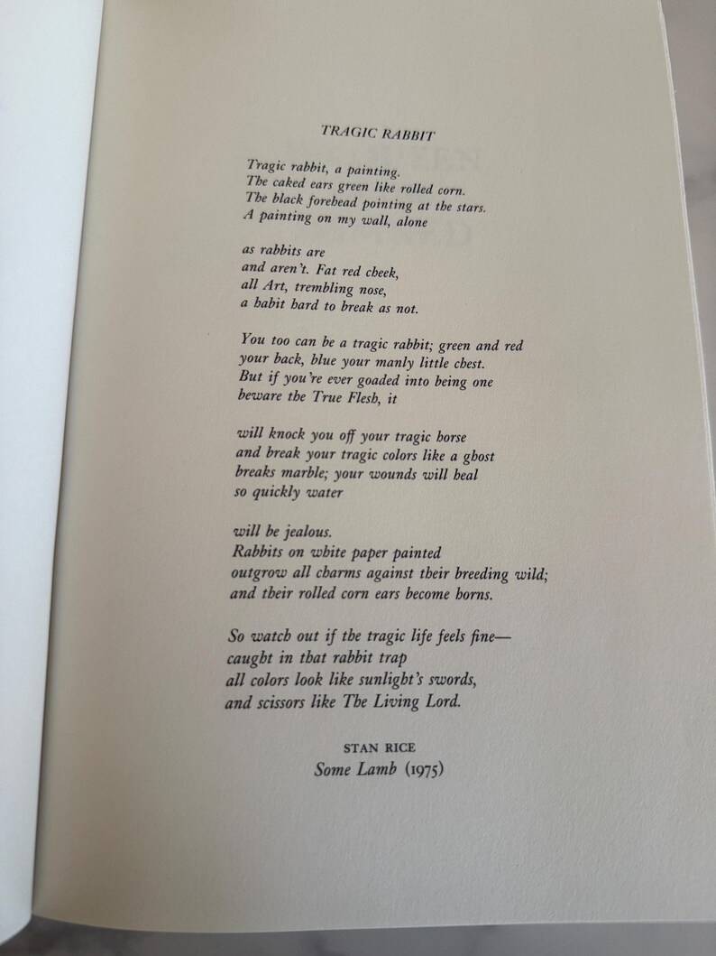 May include: Open book page with the poem "Tragic Rabbit" by Stan Rice. The text is in black font on a cream-colored page. The poem's title and author's name are visible.