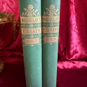 May include: Two green hardcover books titled Macaulay's Essays, Vol. I and Vol. II. The spines feature gold embossed text and floral illustrations. The textured green covers have a cross-hatched pattern with decorative gold lines and borders.