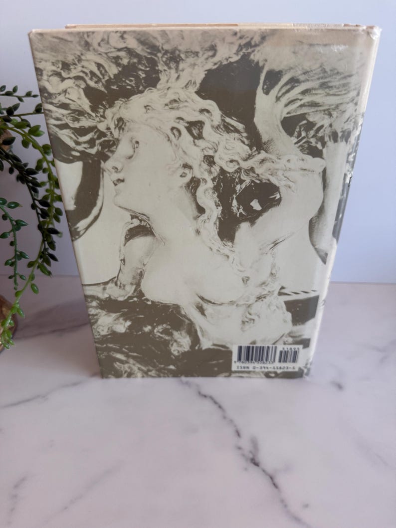 May include: A book with a cover featuring a grayscale illustration of a classical female figure with flowing hair. The artwork is set against a muted background, with the spine visible. The book is wrapped in clear plastic.