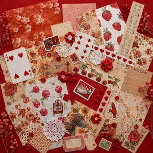 May include: A selection of red and cream-coloured scrapbook paper, playing cards, stickers, and embellishments. The image includes floral patterns, strawberries, cherries, and decorative elements like doilies and buttons. The colour palette is primarily red and cream.