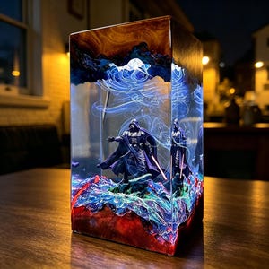 May include: A rectangular resin art piece featuring two Darth Vader figurines. The artwork has a layered design with red, blue, and white accents, and a dark brown top. The figures are set against a backdrop of swirling blue light.