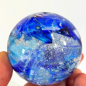May include: A blue glass sphere with silver and white swirls and flecks. The sphere is about the size of a baseball.