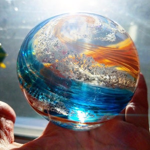 May include: A glass orb with swirling patterns of blue, orange, and white. The orb is made of glass and has a shiny, reflective surface.