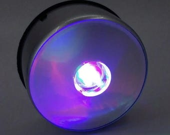 May include: A round, silver-coloured base with a clear, glass-like top. The top is illuminated with a swirling, multi-coloured light, creating a mesmerizing effect.
