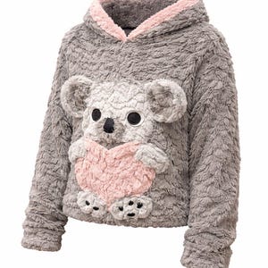 K&ouml;nnte beinhalten: Grauer Kapuzenpullover mit einem Pl&uuml;sch-Koala-B&auml;r-Design auf der Vorderseite. Der Koala hat gro&szlig;e schwarze Augen, eine schwarze Nase und h&auml;lt ein rosa Herz. Das Kapuzenfutter ist rosa.