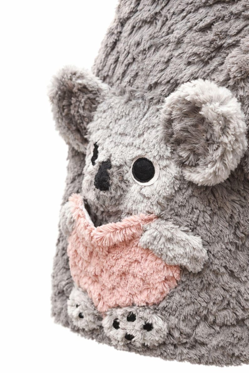 K&ouml;nnte beinhalten: Ein kuscheliges graues Koala-B&auml;r-Spielzeug mit einer rosa Tasche. Der Koala hat gro&szlig;e schwarze Augen, eine schwarze Nase und kleine schwarze Pfoten. Die weiche, pelzige Textur des Koalas ist sichtbar.