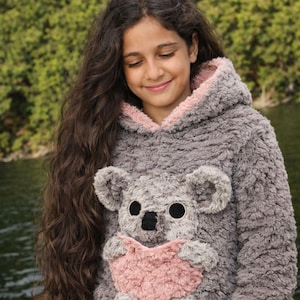 K&ouml;nnte beinhalten: Grauer Kapuzenpullover mit Koala-B&auml;r-Design. Der Koala hat gro&szlig;e schwarze Augen, eine schwarze Nase und eine herzf&ouml;rmige rosa Tasche. Die Kapuze ist mit rosa Stoff gef&uuml;ttert. Der Pullover ist aus weichem, pl&uuml;schigem Material.