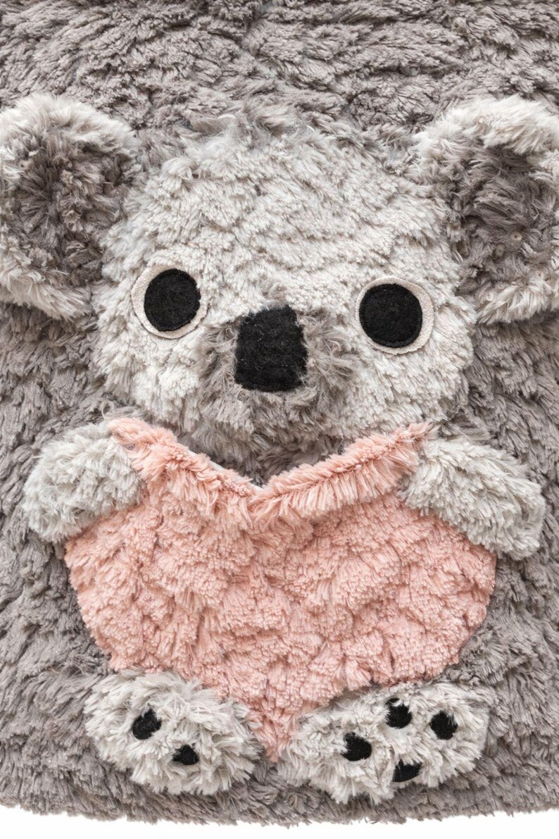 K&ouml;nnte beinhalten: Ein Pl&uuml;sch-Koala mit grauem Fell, gro&szlig;en schwarzen Augen und einer schwarzen Nase. Der Koala h&auml;lt ein herzf&ouml;rmiges Objekt in Rosa. Das Spielzeug hat ein weiches, strukturiertes Aussehen, was auf ein kuscheliges Design hindeutet.