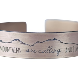 May include: A gold-toned metal bracelet with the inscription "The Mountains are calling and I must go".