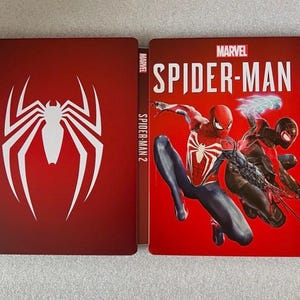 May include: A red and white Spider-Man logo is on the left side of a red game case. The right side features the Marvel Spider-Man 2 game cover with Spider-Man and Miles Morales. The game title is in white.