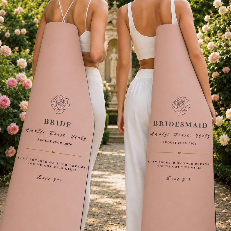 Pu&ograve; includere: Due cartelli nuziali color rosa cipria, uno con la scritta "BRIDE" e l'altro "BRIDESMAID". Ogni cartello presenta un'illustrazione di rosa e il testo: "Amalfi Coast, Italy, August 28-30, 2026". I cartelli includono anche il messaggio "Stay focused on your dreams. You've got this girl! Love you."