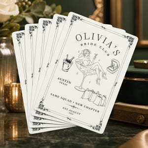 May include: A deck of white playing cards featuring a black line art illustration of a person sitting in a martini glass, a champagne bucket, a ring box, and shopping bags. The text reads OLIVIA'S BRIDE CLUB, AUSTIN TEXAS, SAME SQUAD NEW CHAPTER, EST.AUGUST 2026.