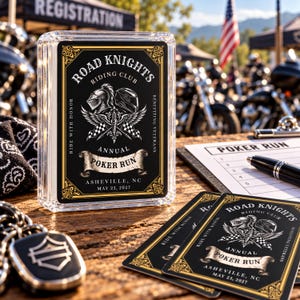 May include: A clear plastic case containing a deck of playing cards with a black and gold design featuring the text Road Knights Riding Club Annual Poker Run Asheville, NC May 23, 2027, alongside two loose cards and a pen.