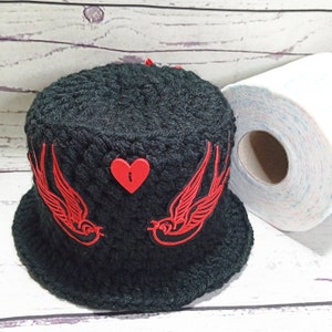 以下が含まれることがあります： 赤い刺繍の鳥と白い鍵穴のデザインの赤いハートが付いた、黒いクロシェのバケットハットです。