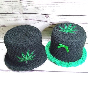 May include: Two black crocheted hats. The left hat features a green embroidered leaf patch on the side. The right hat has a green embroidered leaf patch on top and a green ribbon bow on the side, with a bright green crocheted brim edge.