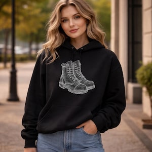 May include: A black hooded sweatshirt featuring a white graphic print of a pair of lace-up work boots on the chest. The hoodie includes a front kangaroo pocket, long sleeves with ribbed cuffs, and a drawstring hood with matching black cords.