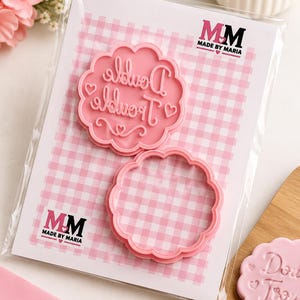 May include: Two pink plastic cookie cutters packaged on a white card with a pink gingham pattern. One cutter features the embossed text Double Trouble with heart accents, while the other is a plain scalloped circle. The brand logo MM Made By Maria is visible.