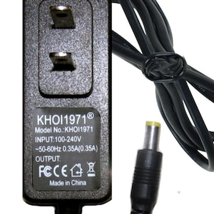 May include: A black AC power adapter with a two-prong wall plug and a cylindrical DC output connector. The label displays KHOI1971, Model No.: KHOI1971, INPUT: 100-240V ~50-60Hz 0.35A(0.35A), OUTPUT, FCC, CE, and Made in China text.
