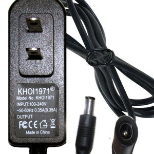 May include: A black power adapter with a two-prong plug and a long cord. The label reads KHOI1971, Model No.: KHOI1971, INPUT: 100-240V ~50-60Hz 0.35A(0.35A), OUTPUT:, FCC, and Made in China. The cord includes a male and female barrel connector plug.