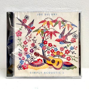 May include: A CD case featuring a colorful illustration with the text "JOE SUZUKI" and "SIMPLY ACOUSTIC 2." The artwork includes birds, flowers, and a ukulele. The color palette includes red, blue, yellow, and green.