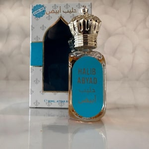 Puede incluir: Un frasco de perfume con una tapa plateada en forma de corona y una etiqueta turquesa que dice "HALIB ABYAD" en inglés y árabe. El frasco contiene un líquido ámbar claro y se presenta con una caja a juego.