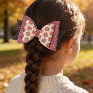 Peut inclure: Un nœud pour cheveux multicouche composé d'un panneau central blanc à motif de citrouilles orange, encadré par deux couches de paillettes roses et une base en paillettes noires. Le nœud est fixé sur une tresse avec une pince décorative.