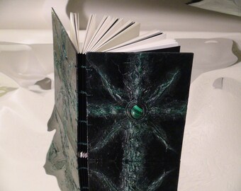 May include: A black leather-bound journal with a green and black marbled cover. A green gemstone is set into the center of the cover.