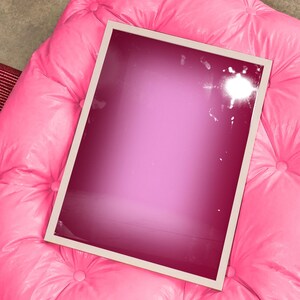 Peut inclure: Un cadre rectangulaire avec une bordure fine de couleur claire contenant une impression en dégradé magenta profond. Le cadre est posé sur un pouf capitonné rose vif doté de plusieurs boutons recouverts de tissu sur sa surface.