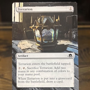 May include: A Magic: The Gathering card titled "Terrarion." The card features an illustration of a detailed, ornate lantern with a landscape visible inside. The card text describes the artifact's abilities and mana costs.