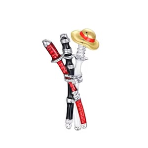 May include: A metal brooch featuring three crossed sword hilts in red, black, and white enamel, bound together by a silver-toned cord detail. A small, gold-coloured straw hat with a red band rests atop the white sword hilt, completing the design.
