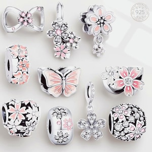 May include: A collection of ten sterling silver charms featuring floral and butterfly motifs. The charms are decorated with pink enamel, clear cubic zirconia stones, and intricate metalwork. Each piece includes a 925 stamp indicating sterling silver.