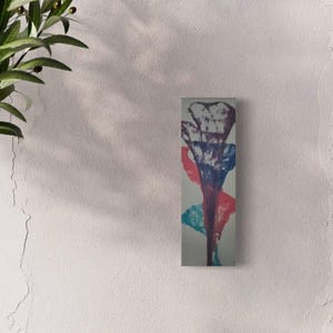 May include: A tall, narrow rectangular wall art piece featuring an abstract design with layered paint strokes in shades of deep purple, vibrant blue, and bright red against a light gray background, displayed vertically on a plain wall surface.