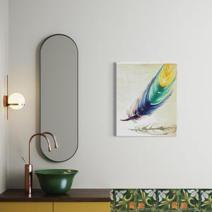 May include: A rectangular wall art print featuring a large, vibrant feather painted in shades of yellow, teal, and deep blue against a light cream background, with a faint, sketched outline of a second feather positioned directly below it.