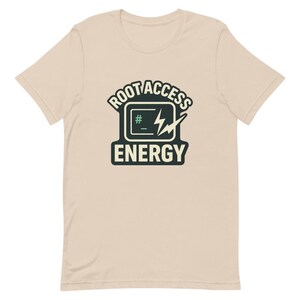 May include: A light tan t-shirt with a graphic that reads "ROOT ACCESS ENERGY". The graphic features a computer screen icon with a lightning bolt and the hash symbol. The shirt is made of a soft material.