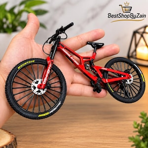 Może przedstawiać: Miniaturowy model czerwonego roweru górskiego z czarnymi oponami z żółtymi napisami, szczegółową ramą z tekstem SIMULATION i H900, czarną kierownicą, czarnym siodełkiem oraz srebrnymi hamulcami tarczowymi na obu kołach, zaprojektowany jako replika.
