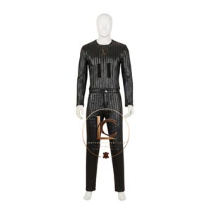 Op de afbeelding: Een zwarte jumpsuit met lange mouwen, voorzien van een verticaal krijtstreepmotief, een ronde halslijn en een getailleerde pasvorm. Het kledingstuk bevat twee rechthoekige zwarte patches op de borst en een cirkelvormig logo met de tekst LEATHERCRAFTEDCOAST.