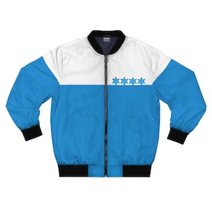 Puede incluir: Chaqueta bomber azul y blanca con cuello, puños y dobladillo negros. La chaqueta presenta una banda horizontal azul con cinco estrellas azules. La parte superior es blanca y las mangas son azules.