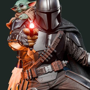 May include: A detailed figurine of The Mandalorian holding a blaster with a red light, with Grogu, also known as Baby Yoda, in his arms. The Mandalorian wears a silver helmet and armor, with a brown belt and pants. Grogu is wrapped in a brown cloth.