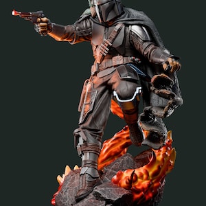 May include: A detailed statue of a character from The Mandalorian. The figure is clad in dark armor, holding a blaster pistol with a red barrel. The statue stands on a rocky base with fiery orange and yellow accents.