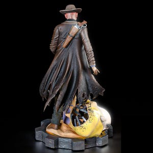 May include: A detailed figurine of a figure in a brown coat and hat, with a gun holster. The figure stands on a gear-shaped base, with a skull and other objects at its feet. The figure is facing away from the viewer.