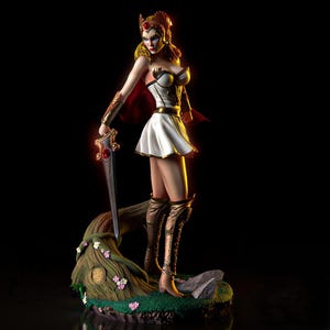 Pode incluir: Figura detalhada de uma guerreira com um traje branco e dourado, segurando uma espada com uma gema vermelha. Ela está em uma base de tronco de árvore com flores. A figura tem uma capa vermelha e botas douradas. O fundo é preto.