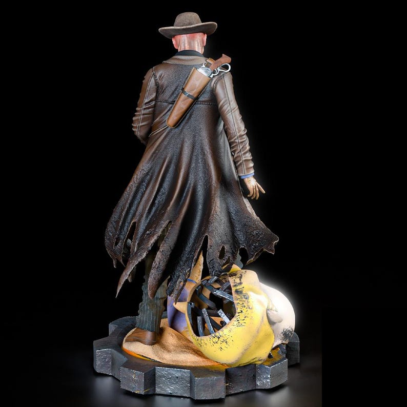 May include: A detailed figurine of a figure in a brown coat and hat, with a holster and gun. The figure stands on a gear-shaped base, with a skull and other elements at its feet. The figure is facing away from the viewer.