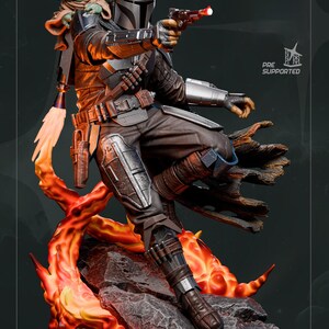 May include: A detailed figurine of The Mandalorian in a dynamic pose, holding a blaster. The figure is clad in dark armor, with a helmet and jetpack. Grogu, also known as Baby Yoda, is perched on his shoulder. The base features fiery orange and red accents.